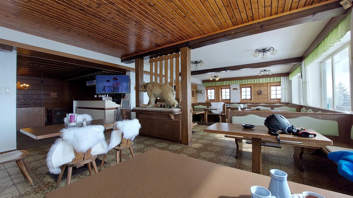 Ein gemütliches Restaurant mit Holzmöbeln und einem rustikalen Ambiente. Auf einem Tisch stehen zwei Tassen und ein Teller, während ein Bär als Dekoration im Hintergrund zu sehen ist. | © TV Hochsteiermark / Brigitte Digruber