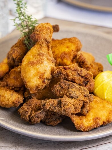 Ein Teller mit knusprigem, frittiertem Hähnchen und Beilagen. Dazu ist eine kleine Zitronenscheibe dekoriert. | © Graz Tourismus - Werner Krug