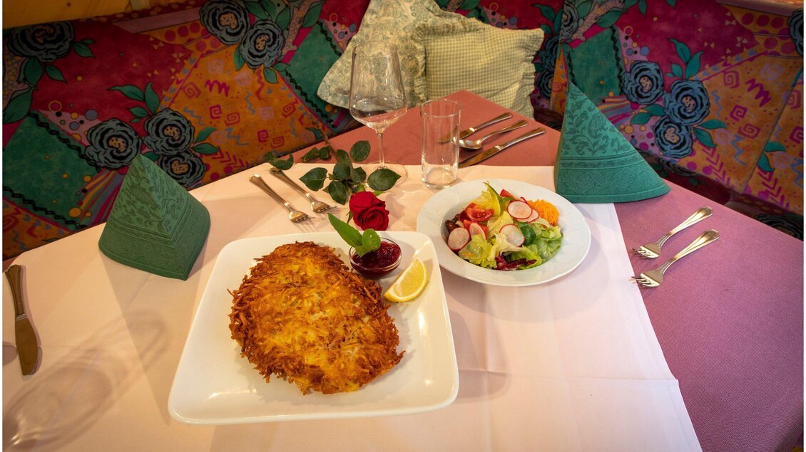 Ein schön gedeckter Tisch mit einer Portion gebratenem Fisch und einem frischen Salat. Die Atmosphäre wird durch die bunten Tischdecken und dekorativen Elemente unterstrichen. | © TV Region Graz - Schwarzbauer