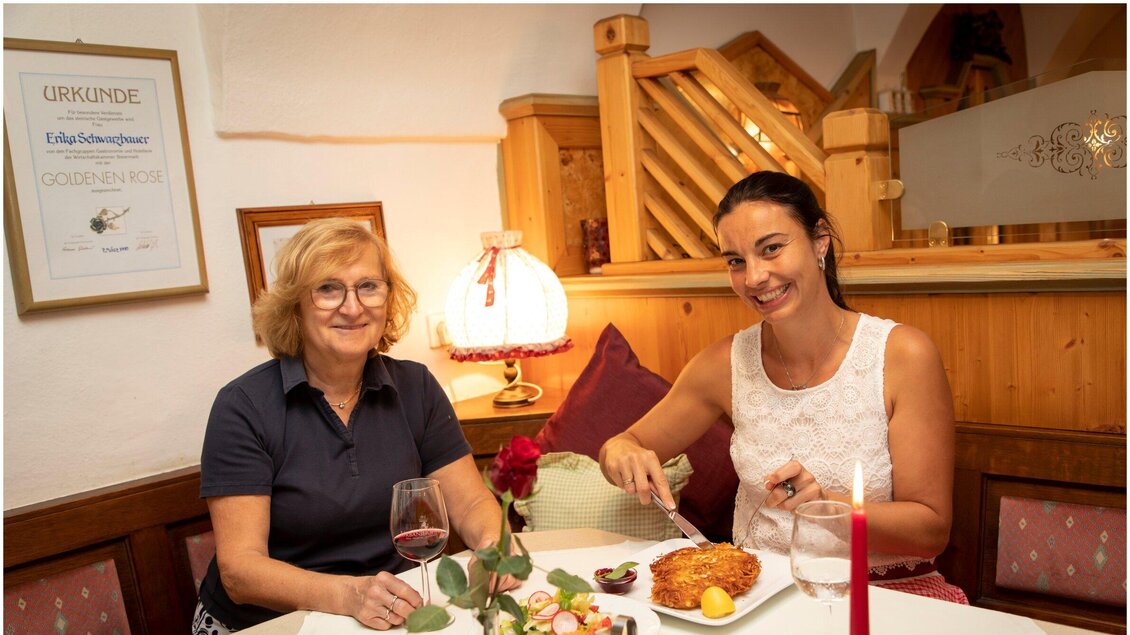 Zwei Frauen sitzen an einem Tisch in einem gemütlichen Restaurant. Sie genießen das Essen und stoßen mit Gläsern an. | © TV Region Graz - Lunghammer