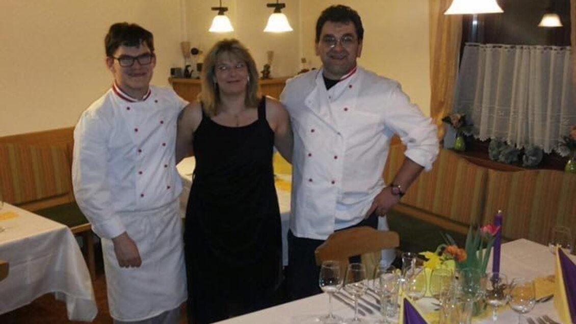 Ein elegantes Restaurant mit gedeckten Tischen und einer warmen Atmosphäre. Drei Personen, darunter Köche inuniform, posieren freundlich für das Foto. | © Gaststätte Franz August