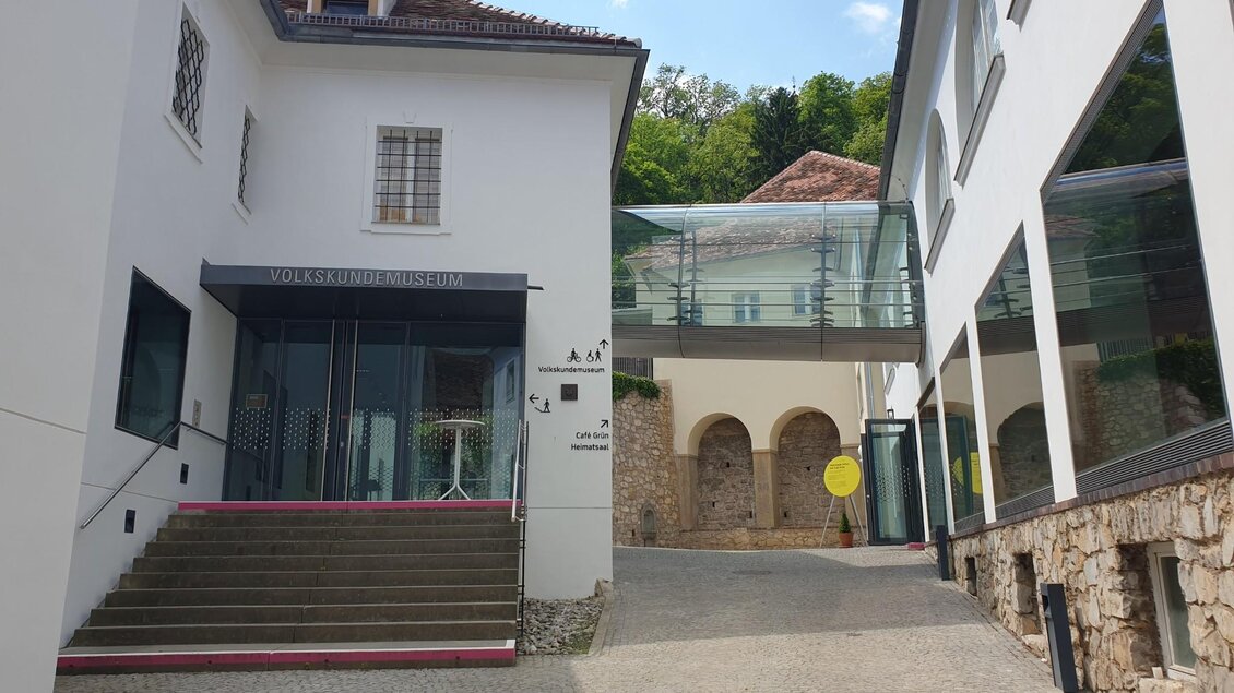 Eingang des Volkskundemuseums mit moderner Glasbrücke und Steintreppen, die zum Haupteingang führen. | © Gudrun Krinzinger, Reisebloggerin