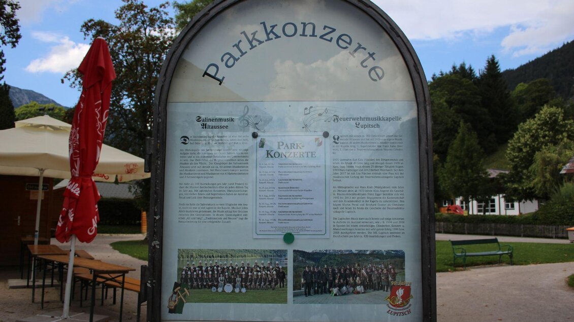 Ein informatives Plakat über Parkkonzerte mit einem Programm und Fotos von Musikern. Im Hintergrund sind Bäume und Sitzgelegenheiten zu sehen. | © Viola Lechner