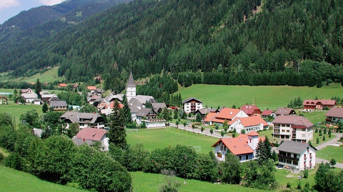 Eine malerische Berglandschaft mit einem kleinen Dorf. Die Häuser sind von grünen Wiesen und Wäldern umgeben. | © Gemeinde Pusterwald