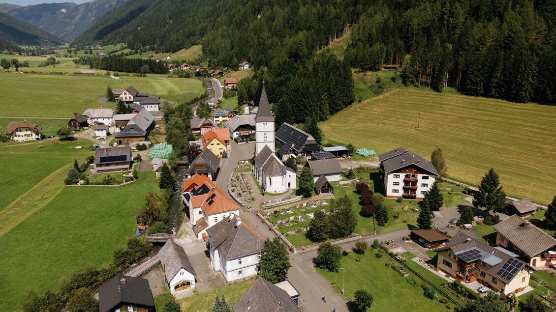 Eine malerische Dorfansicht mit einer Kirche im Zentrum. Umgeben von saftigem Grün und Bergen, zeigt es eine ruhige ländliche Atmosphäre. | © Karl Steinegger