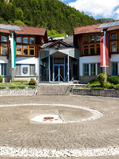 A modern building with wooden and glass elements. It is situated in a green environment and has a circular square in front of it. | © Gemeinde Wörschach