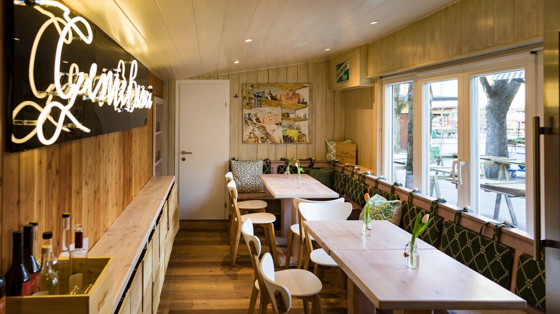 Ein gemütlicher Innenraum mit Holzwänden und hellen Tischen. Dazu eine einladende Atmosphäre mit Pflanzen und einer großen Fensterfront. | © Genießerei am Markt - Werner Krug