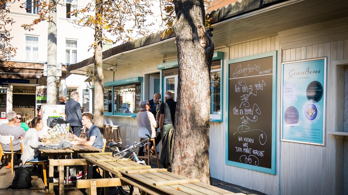 Ein kleines Café mit Außenbestuhlung und einem großen Baum. Menschen genießen die sonnige Atmosphäre. | © Genießerei am Markt