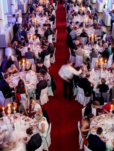 An elegant banquet with festively laid tables and candlelight. Many guests are enjoying dinner in a stylish room with blue lights. | © Edlers
