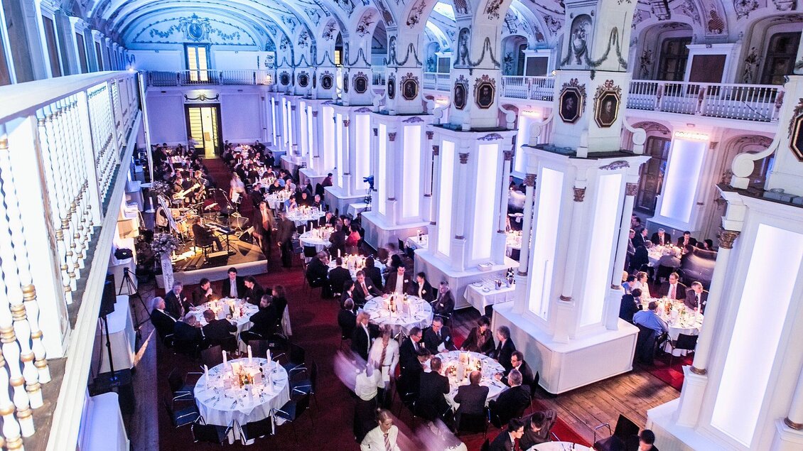 Ein eleganter Saal mit festlich gedeckten Tischen und stimmungsvollem Licht. Die Veranstaltung zieht viele Gäste an, die miteinander interagieren und die Atmosphäre genießen. | © Edlers
