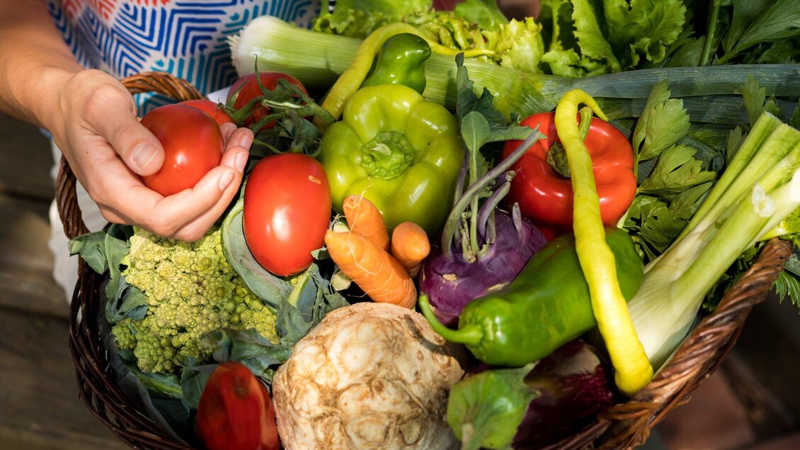 Ein Korb voller frisches Gemüse, darunter Tomaten, Paprika und Brokkoli. Eine Hand hält eine Tomate, während eine bunte Auswahl an Gemüse sichtbar ist. | © Region Graz - Harry Schiffer