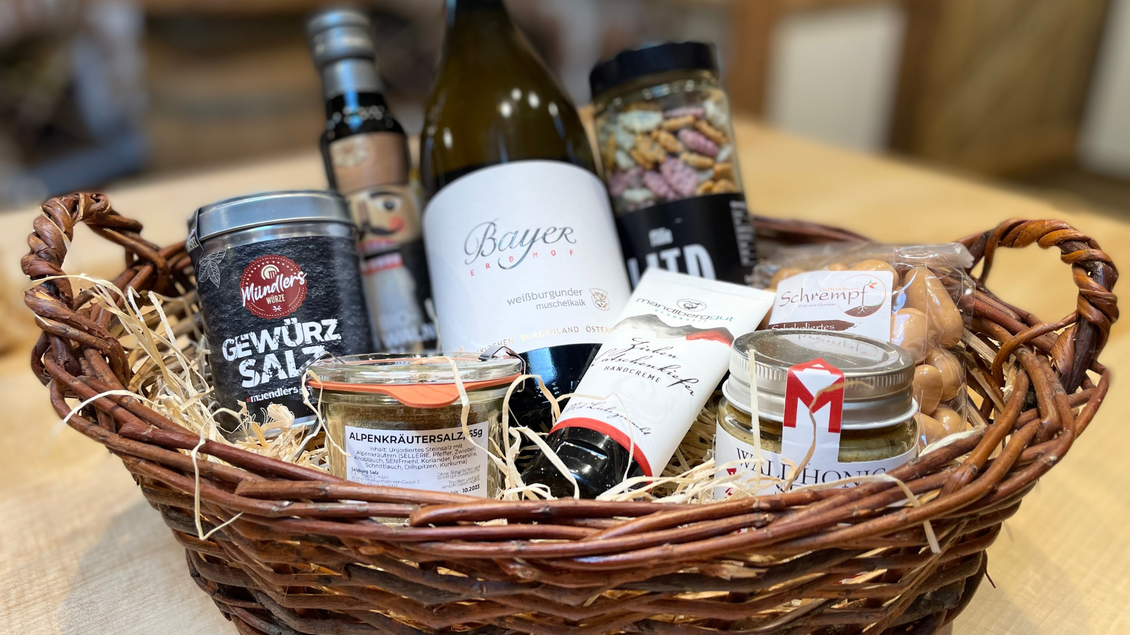 Ein geflochtener Korb mit verschiedenen Lebensmitteln, darunter Gewürzsalz, Wein, Nüssen und Honig. Die Produkte sind ansprechend angeordnet und mit Stroh gefüllt. | © Melanie Jos