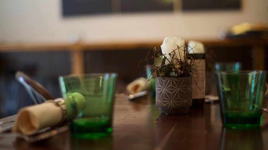 Ein schön gedeckter Tisch in einem Restaurant mit grünen Gläsern und einer dekorativen Blumenmitte. Die Atmosphäre ist warm und einladend. | © Gerüchteküche