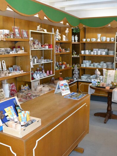 A cozy gift shop with wooden shelves and many decorative items. The sales counter is well-organized and inviting to browse. | © Geschenkestube Walcher