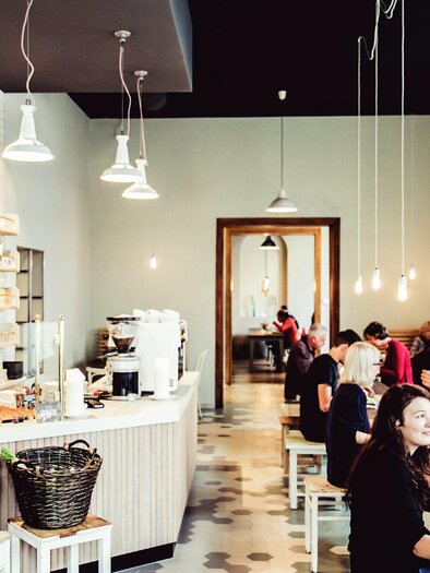 A modern café with a bright interior. Guests are sitting at tables and enjoying drinks and food. | © Ginko - Lupi Spuma