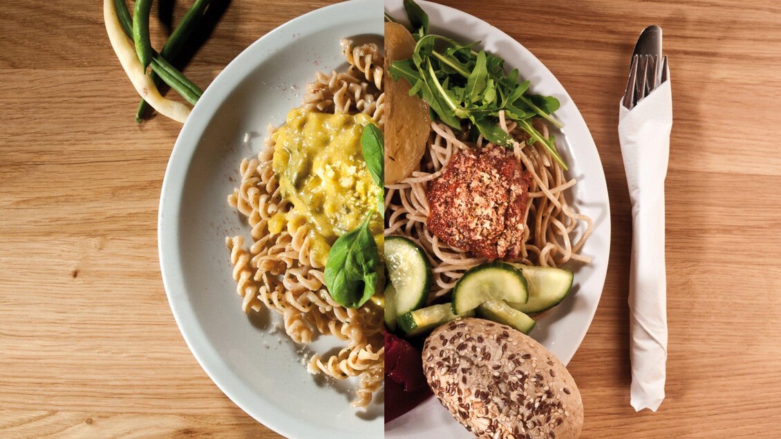 Ein Teller mit zwei verschiedenen Gerichten. Die linke Seite zeigt Nudeln mit Käse, während die rechte Seite gesunde Zutaten wie Salat, Gemüse und ein Brötchen enthält. | © Ginko