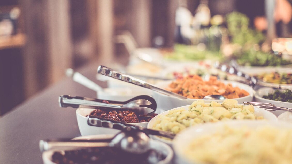 Eine Auswahl an verschiedenen Salaten und Beilagen in weißen Schalen. Es gibt mehrere Löffel zum Servieren. | © Ginko - Lupi Spuma