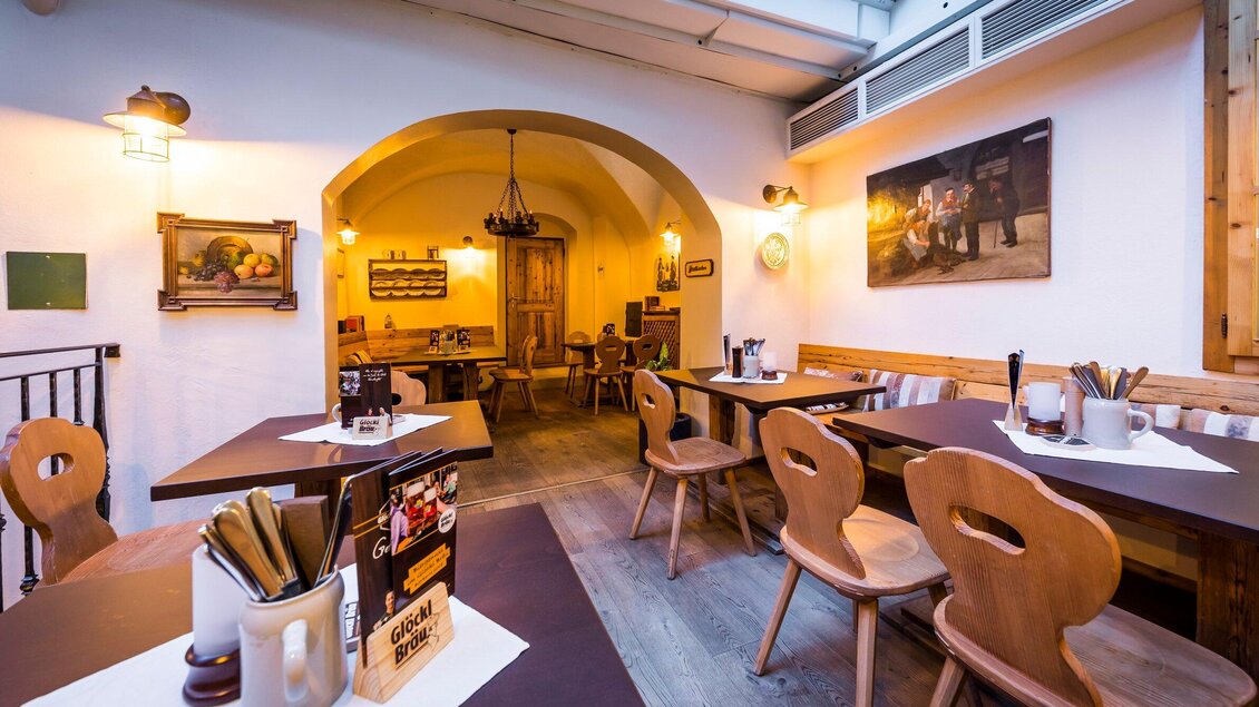 Ein gemütliches Restaurant mit Holzmöbeln und warmem Licht. An den Wänden hängen Gemälde, die eine einladende Atmosphäre schaffen. | © Glöckl Bräu
