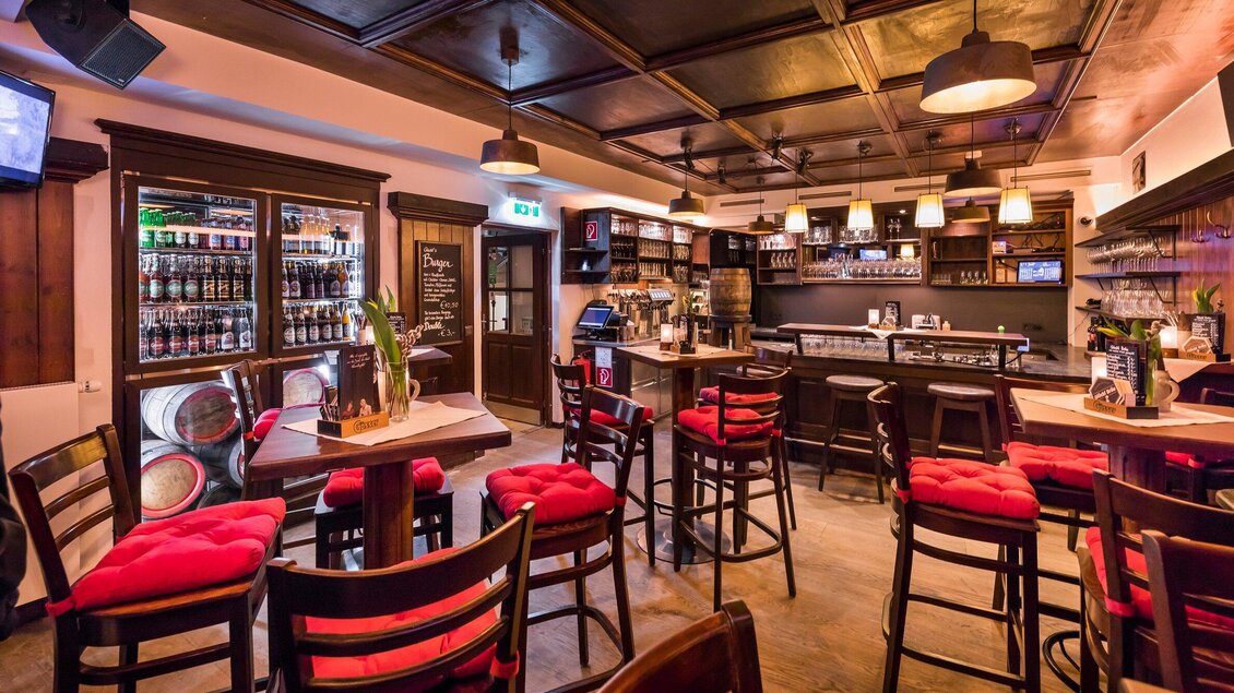 Eine gemütliche Bar mit dunklem Holzinterieur und roten Stühlen. Regale voller Getränke und eine einladende Atmosphäre. | © Glöckl Bräu