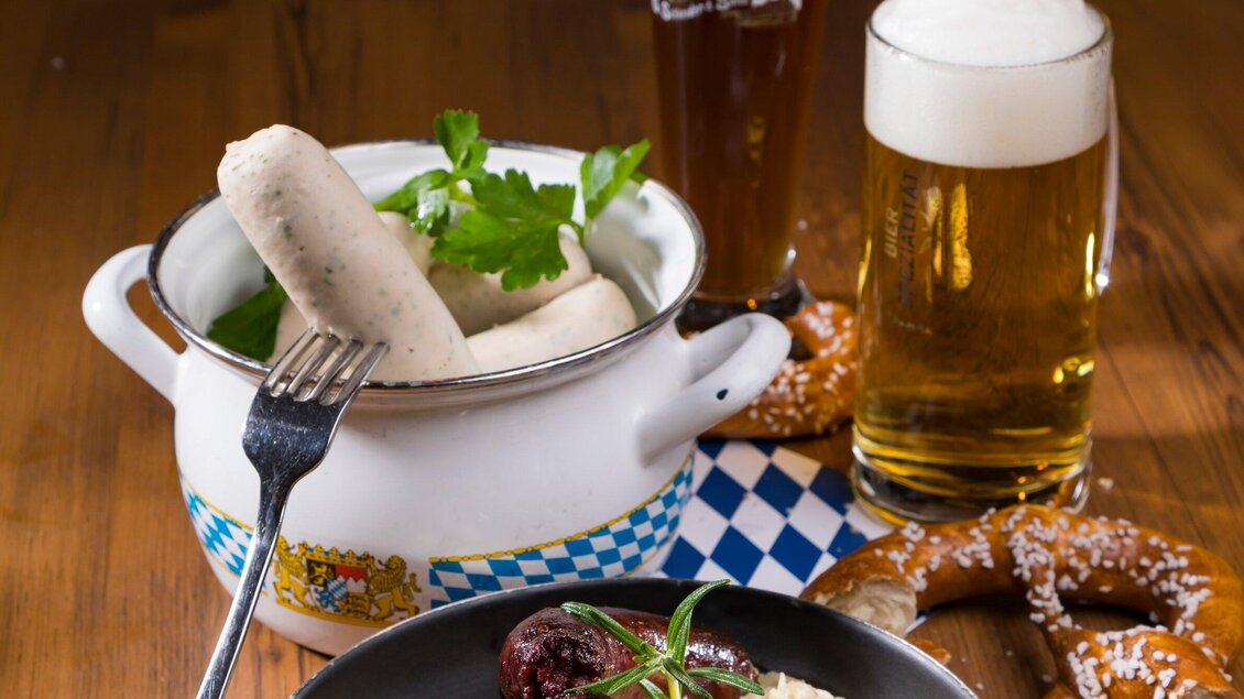 Ein traditionelles bayerisches Gericht mit Weißwürsten, einer Brezel und Bier. Die Speisen sind schön angerichtet und vermitteln eine gemütliche Atmosphäre. | © Glöckl Bräu