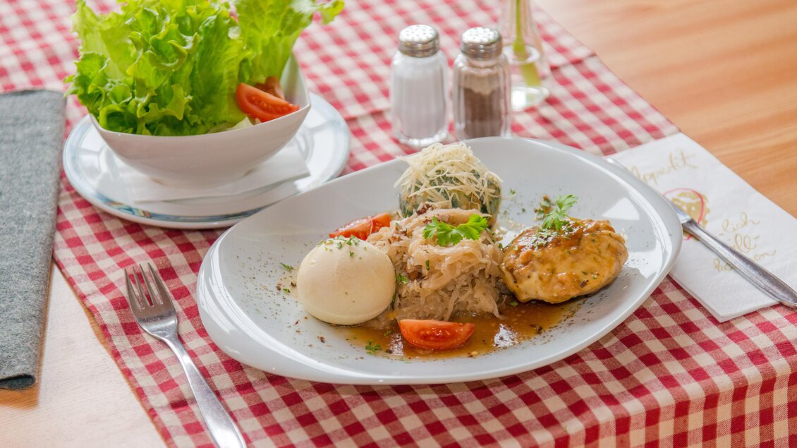 Ein leckeres Gericht auf einem weißen Teller, bestehend aus Fleisch, Beilagen und einem weich gekochten Ei. Dazu eine frische Salatbeilage in einer Schüssel. | © Glösalm
