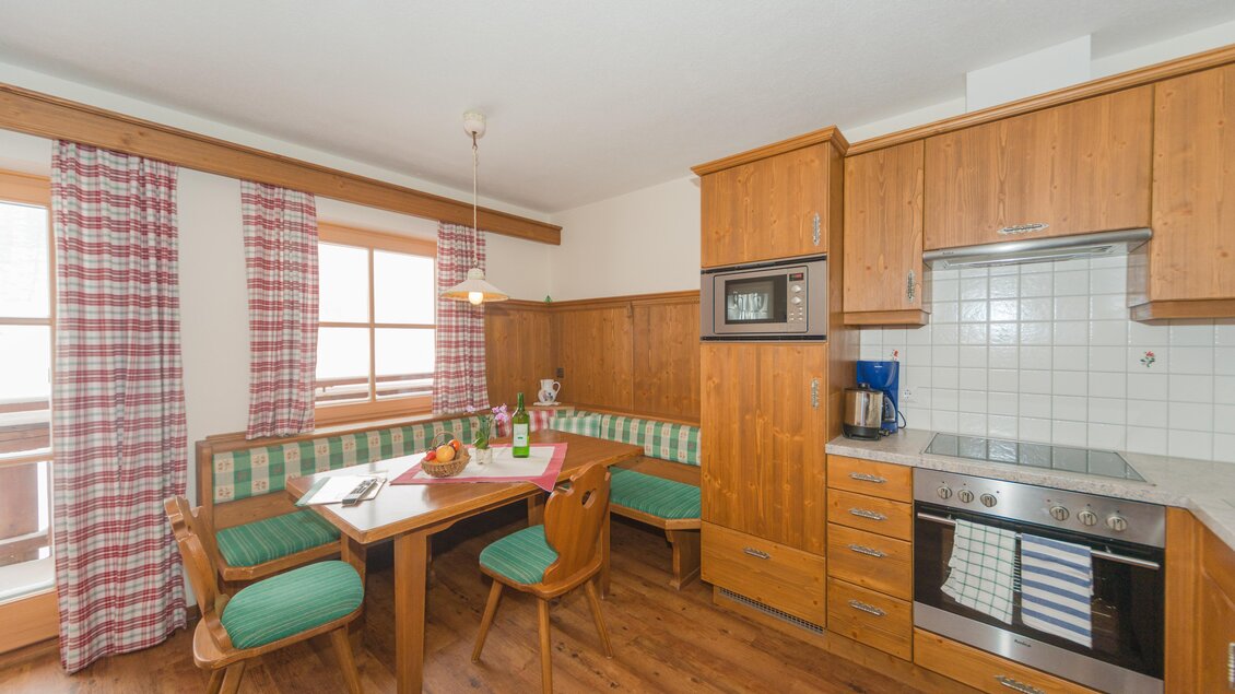 Eine gemütliche Küche mit einem Holztisch und einer Sitzecke. Die Wände sind in warmen Farben gestaltet, und es gibt Fenster mit karierten Vorhängen. | © Glösalm