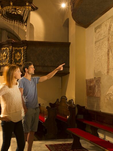 A couple is looking at a mural in a historic church. The surroundings are brightly lit and provide a lovely view of the church's details. | © Bernhard Bergmann
