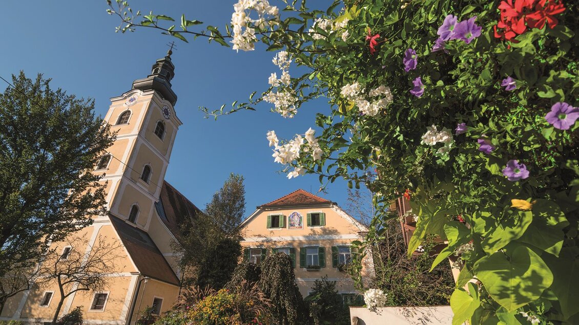 Eine historische Kirche mit einem Turm und schönen Blumen im Vordergrund. Der Himmel ist blau und die Umgebung ist idyllisch. | © Bernhard Bergmann