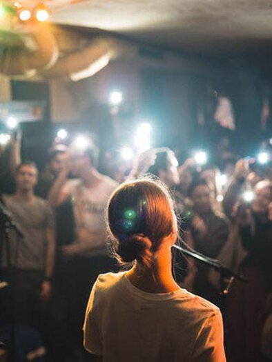 Eine Sängerin steht auf der Bühne und tritt vor einem begeisterten Publikum auf. Die Zuschauer halten ihre Telefone in die Höhe und filmen das Konzert. | © Glam Feldbach