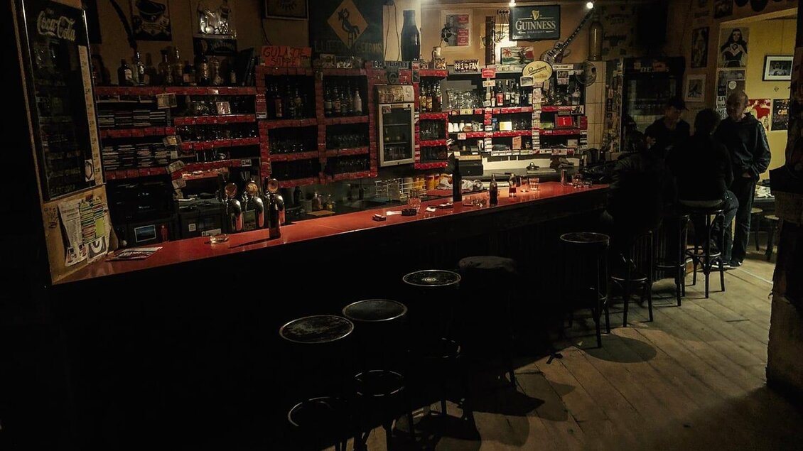 Eine gemütliche Bar mit einem langen Holztresen und wenigen Gästen. Im Hintergrund sind Regale mit Getränken und dekorativen Elementen. | © Glam Feldbach