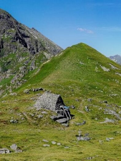 Eine weitläufige Berglandschaft mit grünen Wiesen und hohen Gipfeln. Der Himmel ist klar und blau, ideal für Wanderungen in der Natur. | © Roland Gutwenger