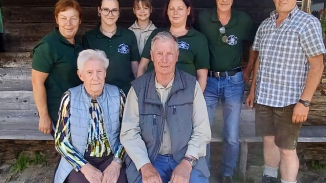Eine Gruppe von acht Personen steht vor einem Holzgebäude. Sie lächeln und tragen jeweils lässige Kleidung. | © Fam. Lipp