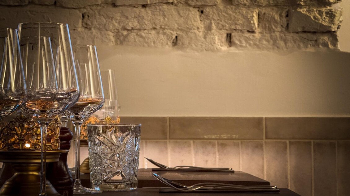 Tischgedeck mit Weingläsern und einem Kristallglas, vor einer hellen, gemauerten Wand. | © Glockenspielkeller