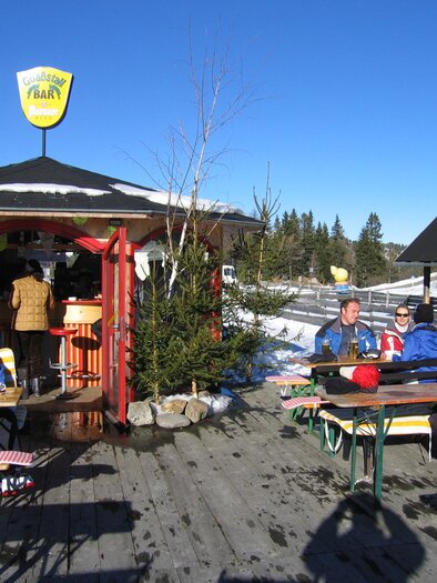 A cozy ski hut with seating in the snow. Guests enjoy the sun under a clear blue sky. | © Schlosshotel Seewirt
