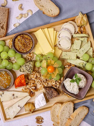 Eine appetitliche Käseplatte mit Trauben, Nüssen und verschiedenen Brotsorten. Die Anordnung ist ansprechend und lädt zum Genießen ein. | © Goldplatzl