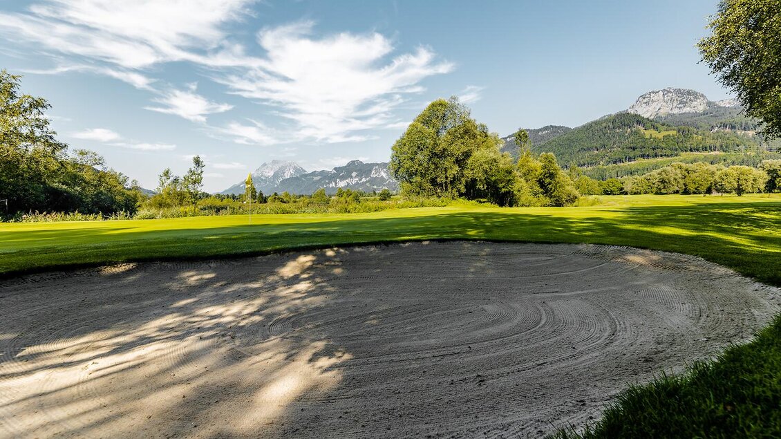 Ein ruhiger Golfplatz mit einer Sandbunker und einer malerischen Bergkulisse im Hintergrund. Der Himmel ist blau und die Landschaft ist grün und einladend. | © Thomas Sattler