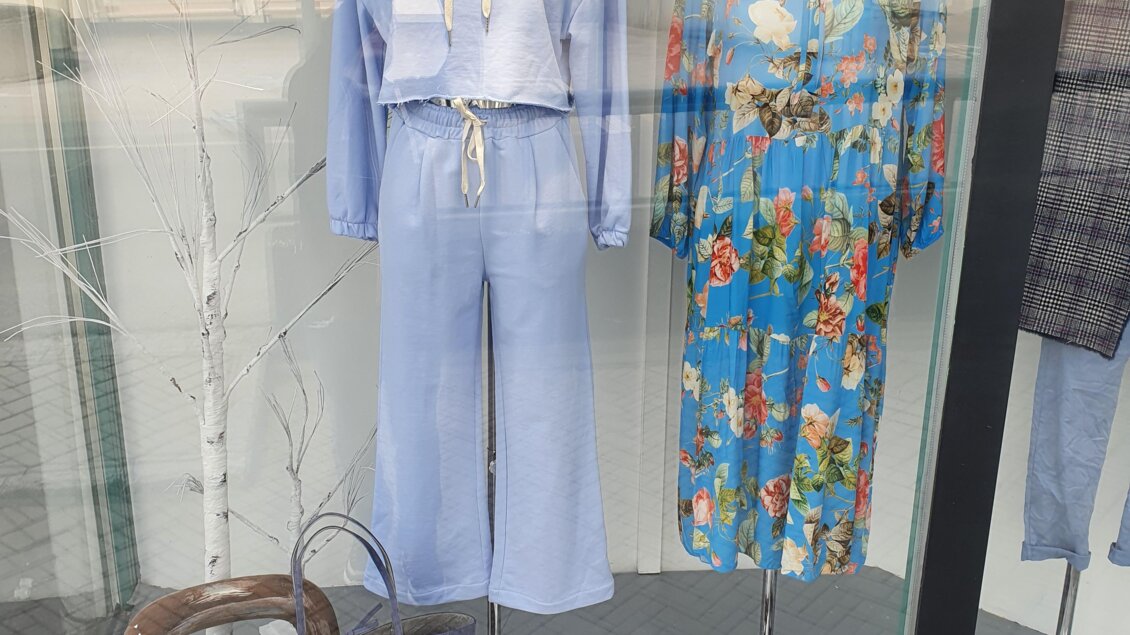 Eine Schaufenster-Auslage mit modischer Kleidung. Links ist ein lässiger blauer Hoodie mit einer passenden Hose, rechts ein farbenfrohes Kleid mit Blumenmuster. | © Golf-Fashion-Lifestyle Judith Schraberger
