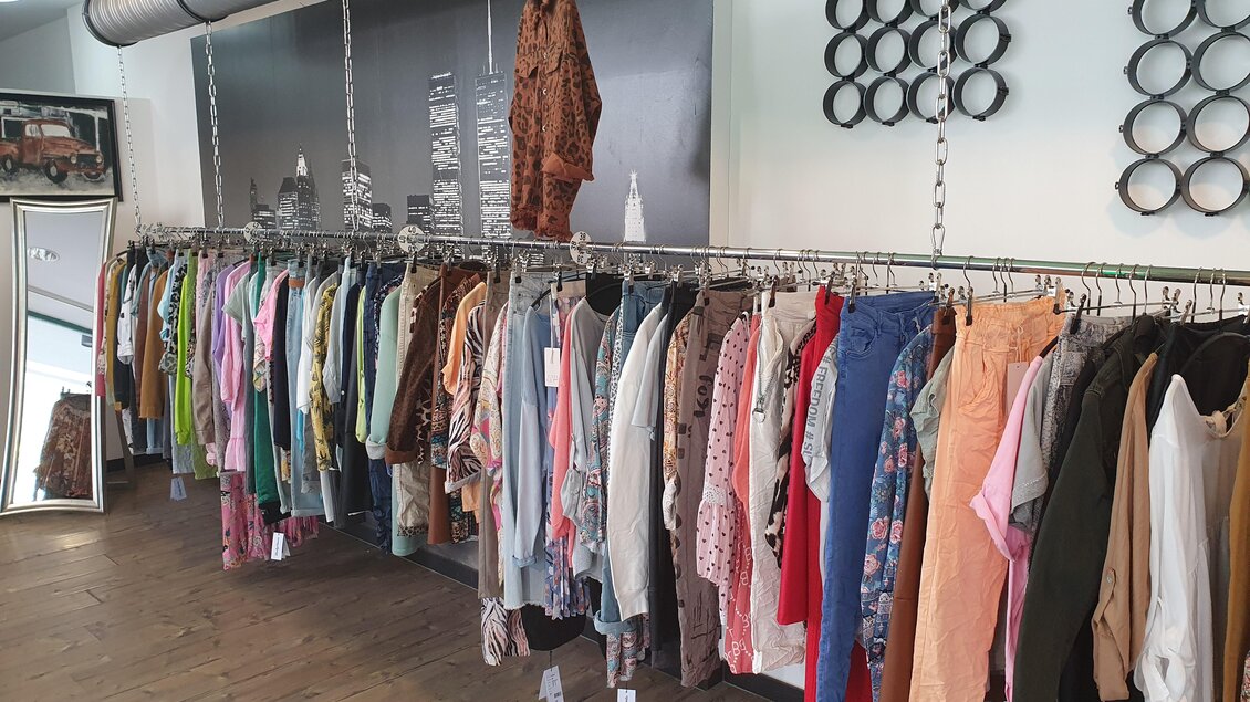 Ein Modegeschäft mit einer Auswahl an Kleidung auf Ständern. Die Wände sind modern gestaltet und es gibt einen Spiegel im Raum. | © Golf-Fashion-Lifestyle Judith Schraberger