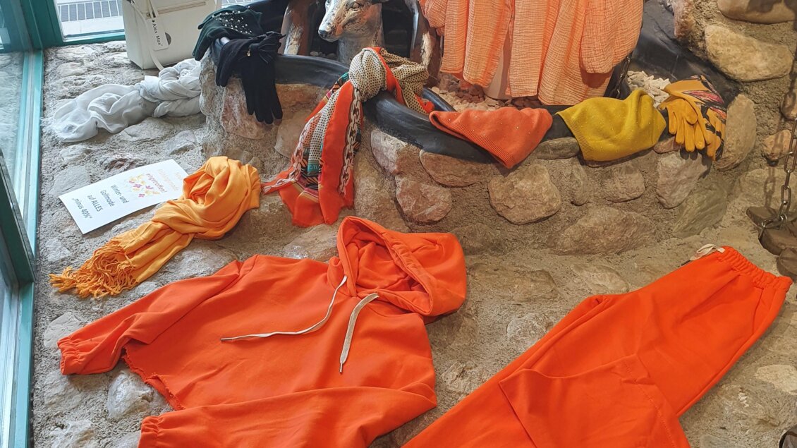 Ein Schaufenster mit orangefarbener Kleidung, darunter ein Hoodie und eine Bluse, sowie passende Accessoires. Die Kleidung ist kreativ und stilvoll präsentiert. | © Golf-Fashion-Lifestyle Judith Schraberger