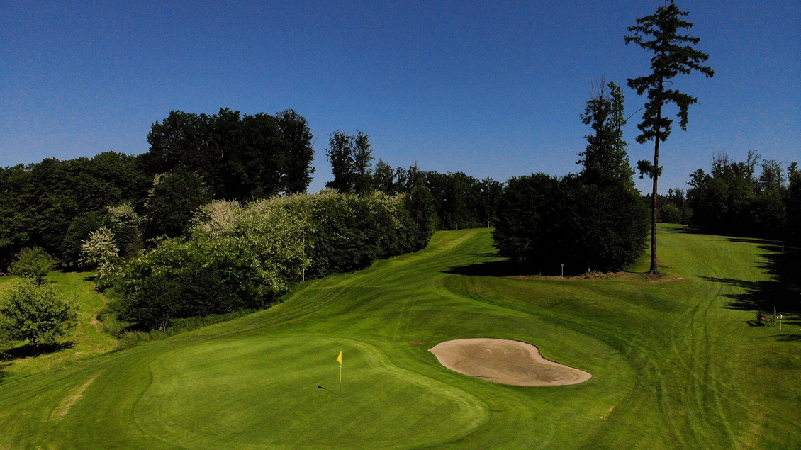 Eine Golfanlage mit grünem Rasen und einem Sandbunker. Im Hintergrund sind Bäume und ein blauer Himmel zu sehen. | © GEPA-pictures - Murhof Gruppe