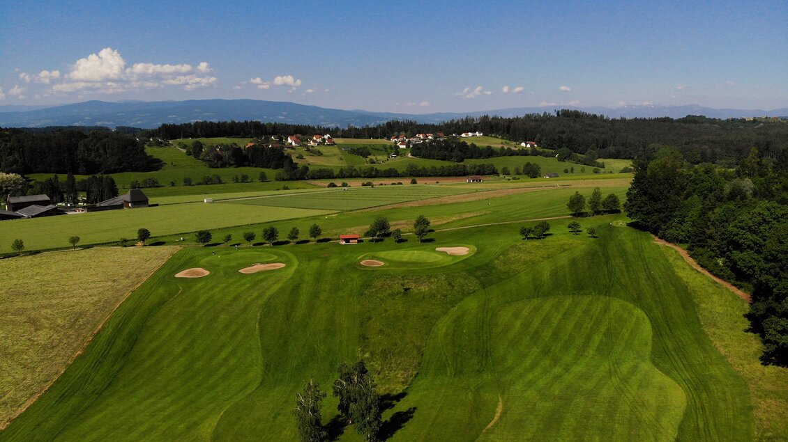 Eine grüne Golfplatzlandschaft mit verschiedenen Spielbereichen. Im Hintergrund sind sanfte Hügel und ein klarer Himmel zu sehen. | © GEPA Pictures