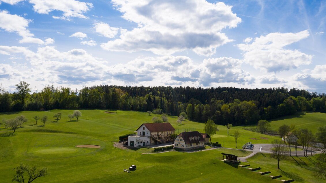Eine grüne Golfanlage mit einem charmanten Bauernhaus und leicht bewaldeten Hügeln. Der Himmel ist blau mit einigen weißen Wolken. | © GEPA Pictures