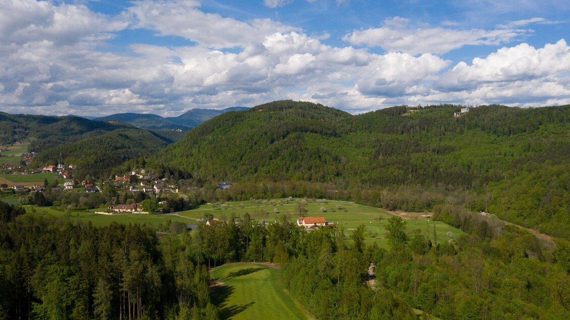 Eine wunderschöne Landschaft mit sanften Hügeln und üppigem Grün. Kleine Häuser sind in der Ferne zwischen den Bäumen sichtbar. | © GEPA-pictures - Murhof Gruppe