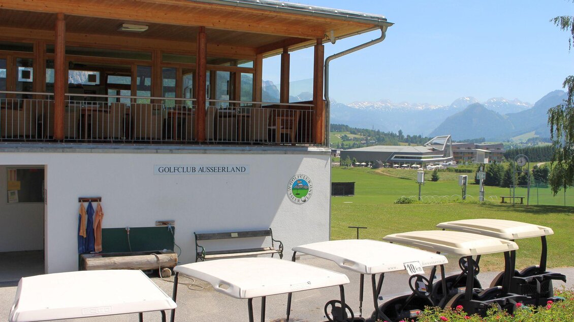 Ein Golfplatz mit einem modernen Clubhaus und mehreren Golfwagen. Im Hintergrund sind grüne Wiesen und Berge zu sehen. | © TVB Ausseerland - Salzkammergut_Viola Lechner