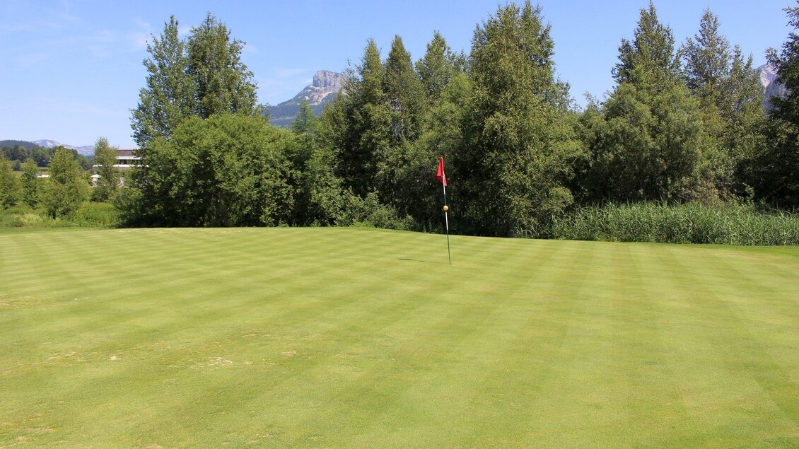 Eine gepflegte Golfplatzlandschaft mit grünem Rasen und vereinzelten Bäumen. Im Hintergrund sind einige Berge und ein blauer Himmel sichtbar. | © TVB Ausseerland - Salzkammergut_Viola Lechner