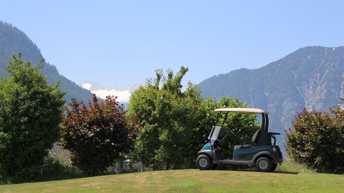 Ein Golfwagen steht auf einem grünen Rasen vor einer malerischen Berglandschaft. Die Umgebung ist von Bäumen und Sträuchern gesäumt. | © TVB Ausseerland - Salzkammergut_Viola Lechner