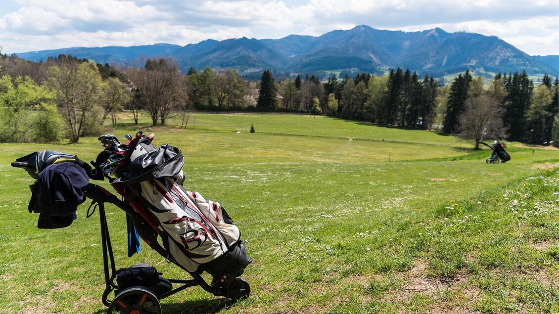 Ein Golfwagen steht auf einem grünen Golfplatz mit einer schönen Berglandschaft im Hintergrund. Die Wolken ziehen locker am Himmel vorbei. | © Golfclub Schloss Feistritz
