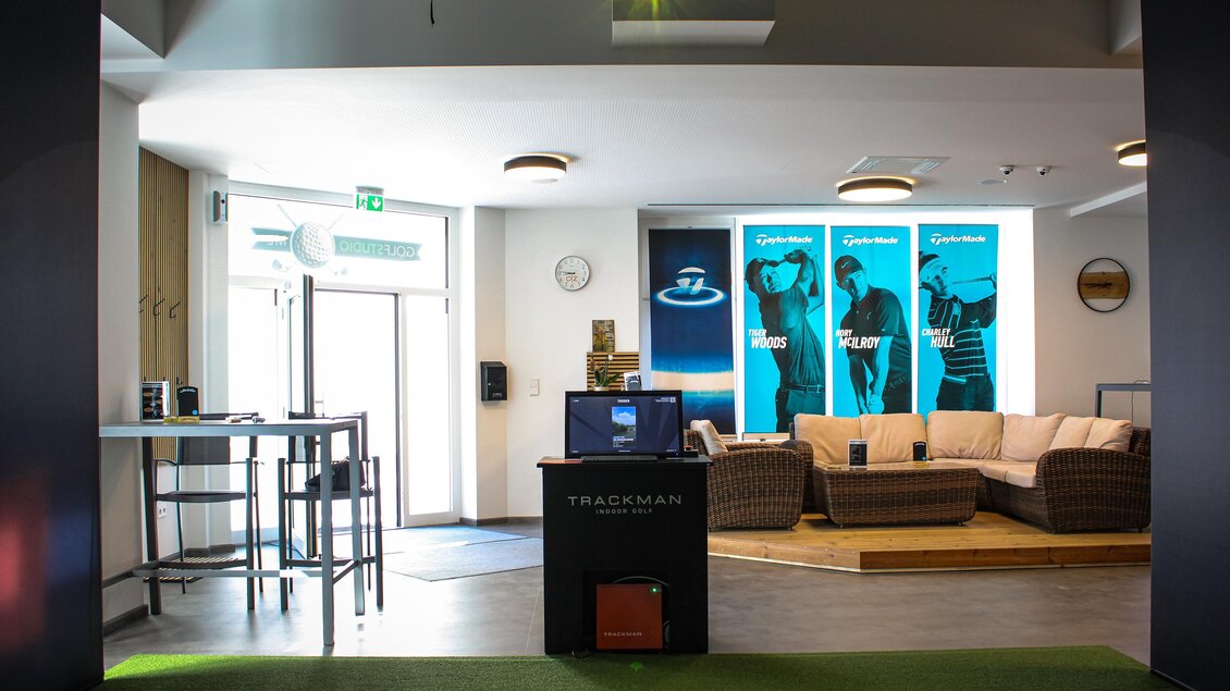 Ein modernes Golf-Trainingsstudio mit einem Empfangstresen und gemütlichen Sitzgelegenheiten. An den Wänden sind große Bilder von Golfern zu sehen. | © Golfstudio ML