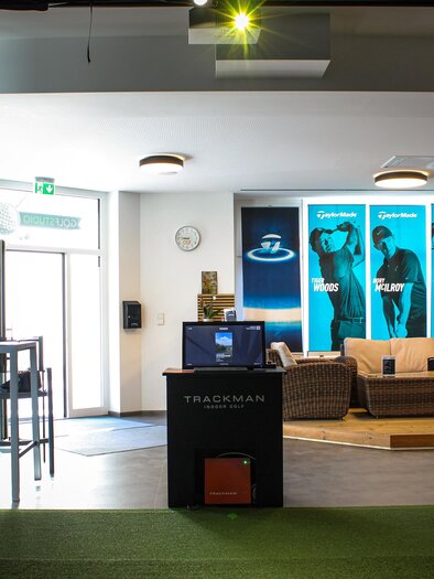 A modern golf training studio with a reception desk and cozy seating areas. Large pictures of golfers can be seen on the walls. | © Golfstudio ML