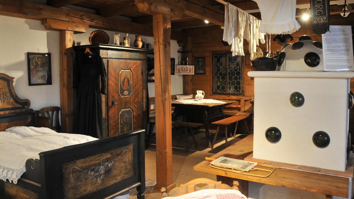 Ein traditionelles Zimmer mit einem schönen Holzbett, einer Kommode und einem Esstisch. An den Wänden hängen alte Kleidungsstücke und Dekorationen. | © Gröbming Museum